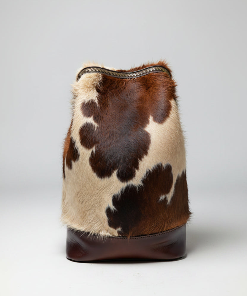 Brown and beige cowhide backpack with leather straps on a gray background