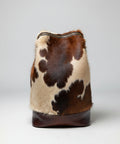 Brown and beige cowhide backpack with leather straps on a gray background